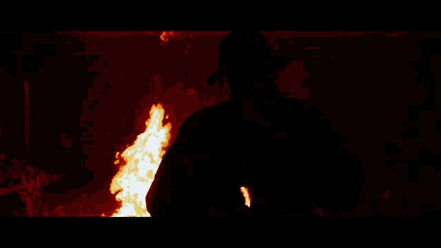 a man in a hat stands in front of a fire