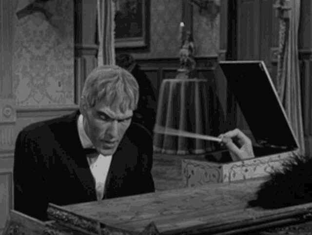 a man in a tuxedo is holding a piece of paper in his hand while sitting at a piano .