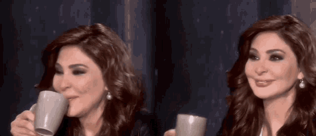 a woman is drinking a cup of coffee and smiling while another woman looks on .