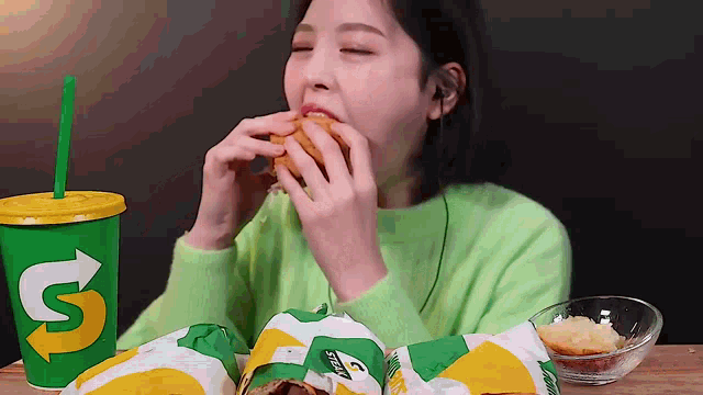 a woman in a green sweater is eating a subway sandwich