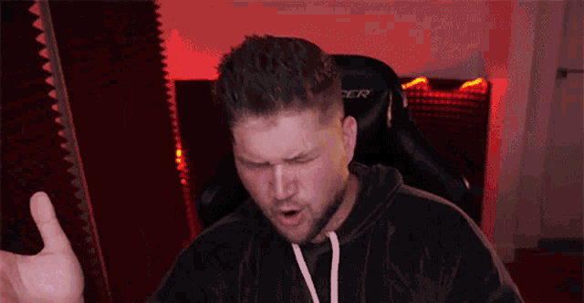 a man in a black hoodie is giving a thumbs up in front of a chair that says dxracer