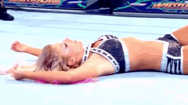 a female wrestler is laying on the floor in a wrestling ring .