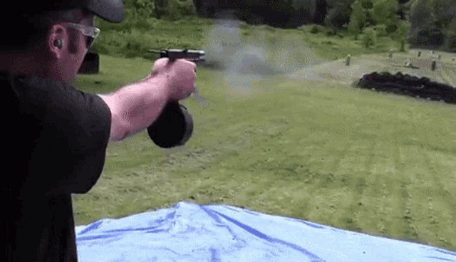 a man is shooting a gun in a field while wearing sunglasses and ear buds .