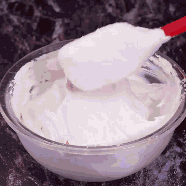 a bowl of whipped cream is being stirred with a red spatula