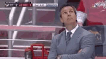 a man in a suit and tie is sitting in the stands with his arms crossed .