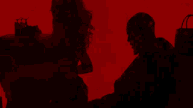 a man and a woman are standing in a dark room with a red background