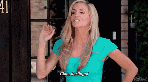 a woman in a blue shirt is standing in front of a door and says ciao darlings