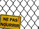 a yellow sign that says ne pas nourrir is hanging on a chain link fence