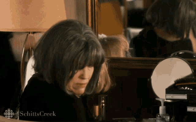 a woman looking at herself in a mirror with schitts creek written on the bottom