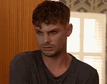 a man with curly hair is wearing a black shirt and making a funny face .