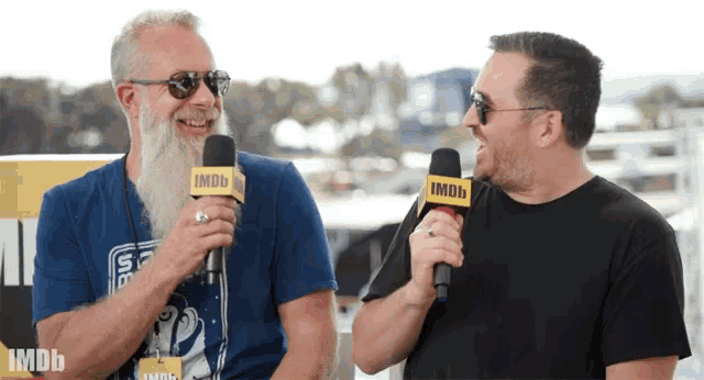 a man with a beard is laughing while talking into an imdb microphone