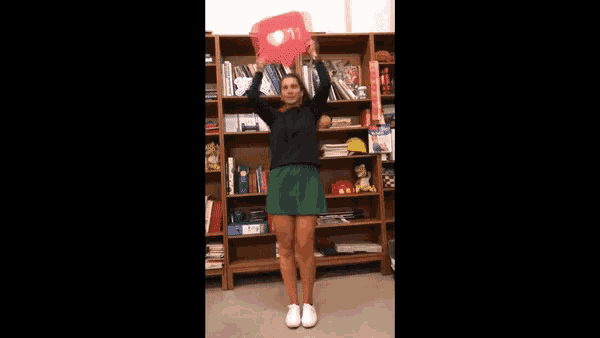 a woman in a green skirt is holding a red heart shaped object in her hands .