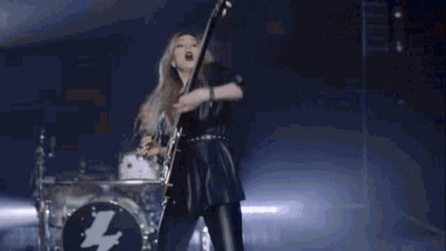 a woman playing a guitar on a stage with a lightning bolt in the background