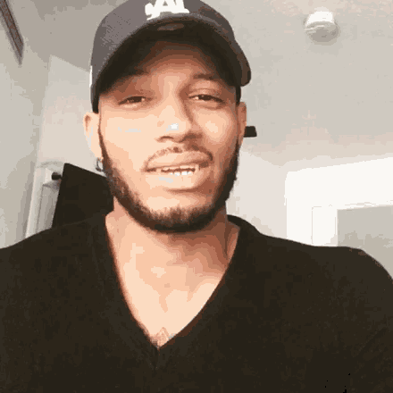 a man with a beard wearing a hat and a black shirt is smiling .