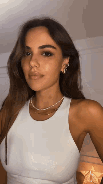 a woman wearing a white tank top and pearls