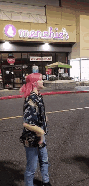 a woman with pink hair is walking down the street in front of a restaurant called menchie 's