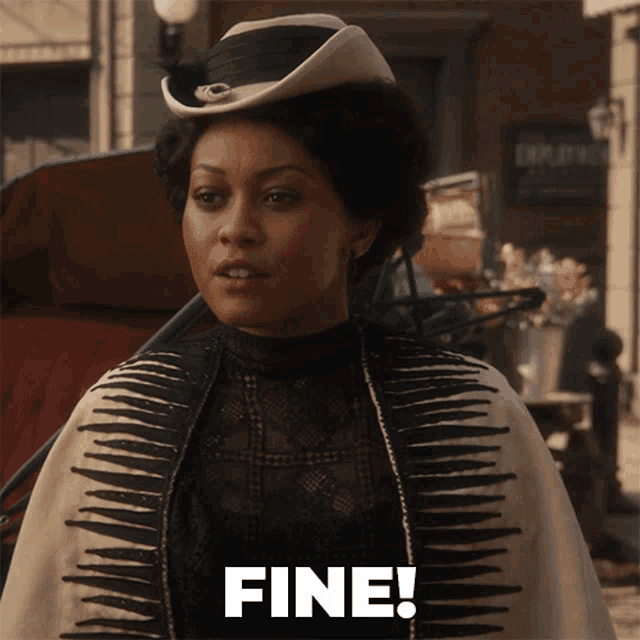 a woman wearing a hat and a cape is standing in front of a sign that says fine