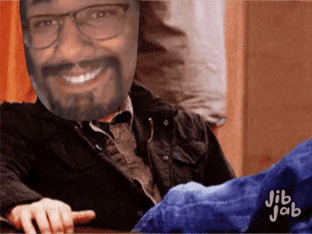 a man with glasses and a beard is smiling and pointing his finger