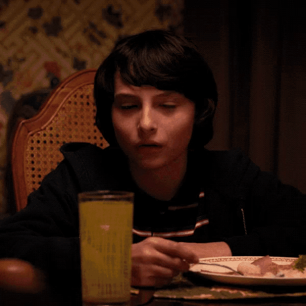 a young boy sits at a table with a glass of orange juice