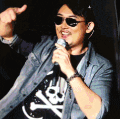 a man singing into a microphone wearing sunglasses and a skull and crossbones shirt