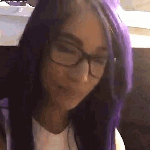 a woman with purple hair and glasses is making a face .