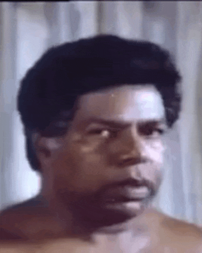a man without a shirt is making a funny face while looking at the camera .