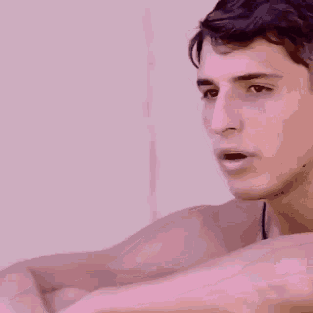 a close up of a shirtless man 's face against a pink background .