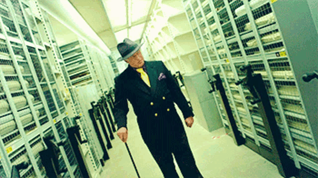 a man in a black suit and purple tie is walking down a hallway holding a cane