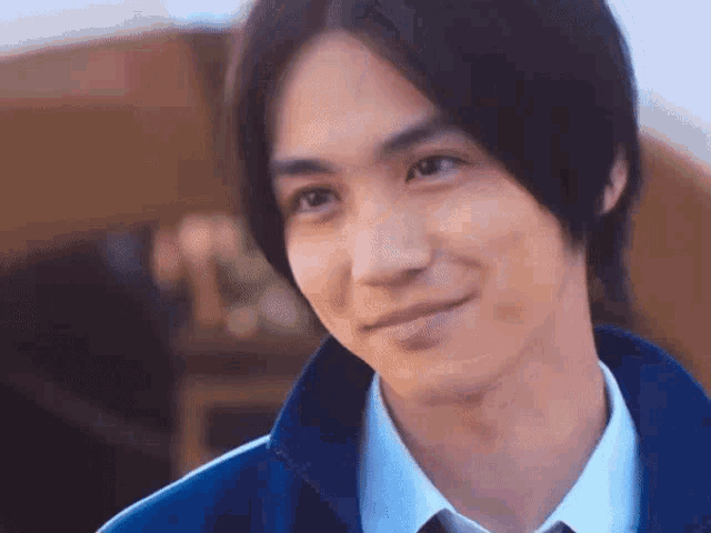 a close up of a young man wearing a blue jacket and tie smiling .