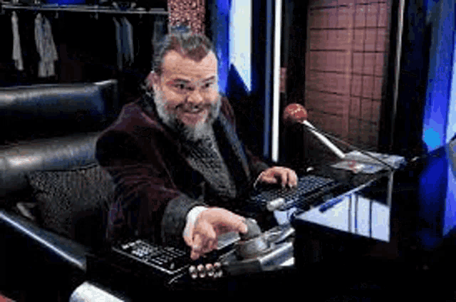 a man with a beard is sitting in a chair at a desk with a keyboard .