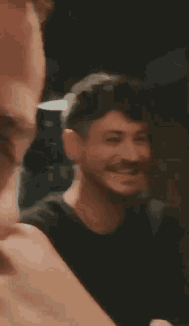 a man with a beard is smiling in a blurry photo while a woman looks on .