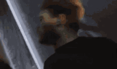 a man with a beard is standing in a dark room with a light shining on his face .