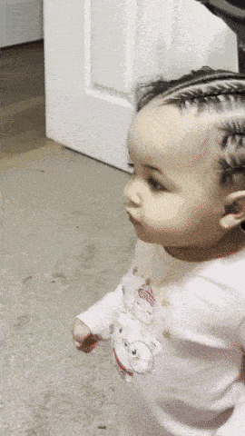 a baby with braids is wearing a white shirt with a teddy bear on it
