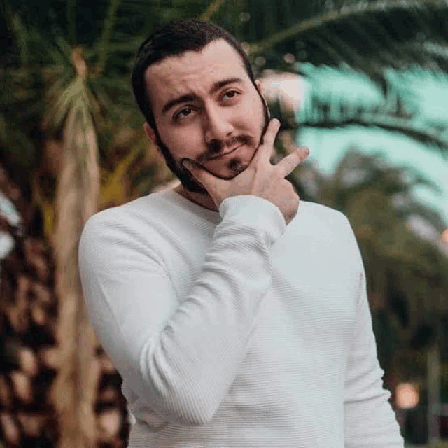 a man with a beard is holding his hand to his chin and making a funny face .