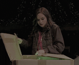 a woman in a denim jacket is opening a cardboard box with a green light behind her
