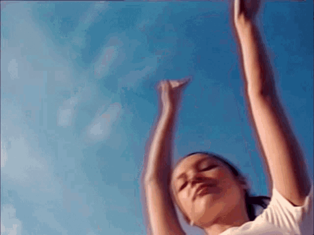 a woman is dancing with her arms in the air against a blue sky .