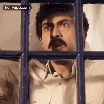 a man with a mustache is looking out of a window with his mouth open .