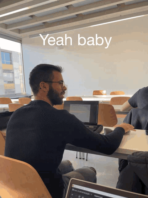 a man sits at a desk in front of a laptop with the words yeah baby above him