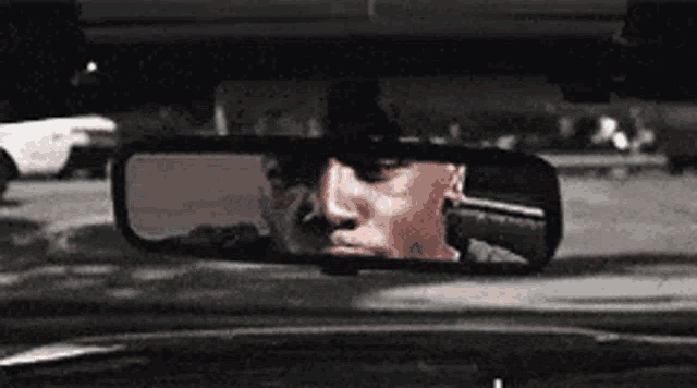a man is reflected in the rear view mirror of a car .