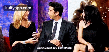 a man in a suit and tie sits next to two women and says lisa david say something ..