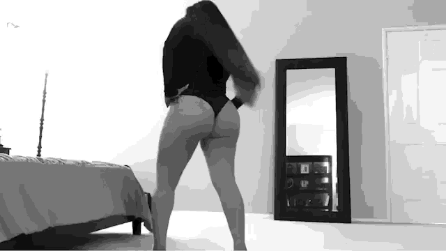 a woman in a black bodysuit is dancing in front of a mirror in a bedroom .