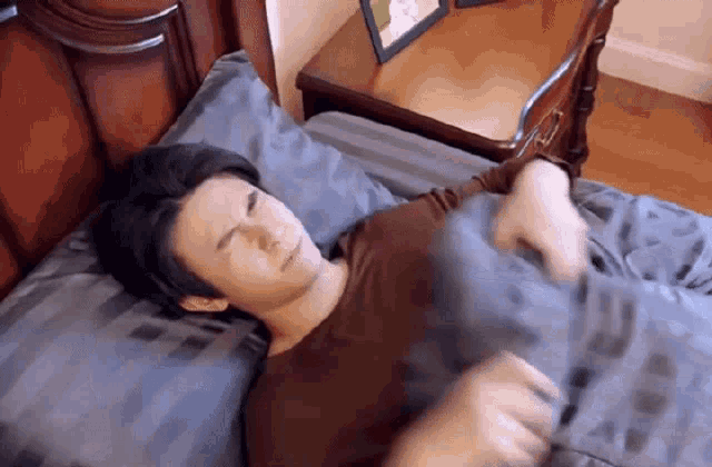 a man in a brown shirt is laying in a bed with a pillow .