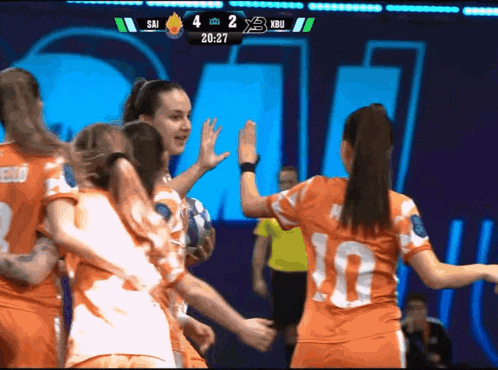 a group of female soccer players high five each other in front of a scoreboard