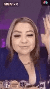 a woman is smiling and waving at the camera while sitting in front of a purple background .