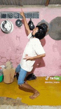 a man wearing a helmet is dancing in front of a pink wall with pots and pans on it