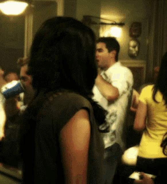 a group of people are gathered in a room and one of them is wearing a yellow shirt