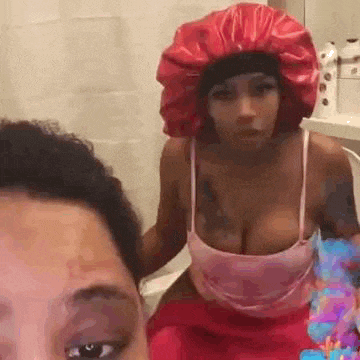 a woman wearing a red hat is sitting on a toilet next to another woman wearing a pink tank top .