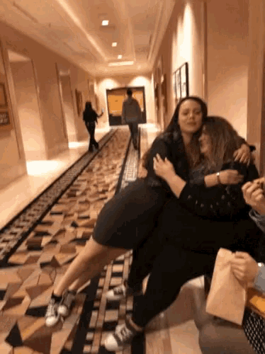 two women are hugging in a hallway while a man walks behind them
