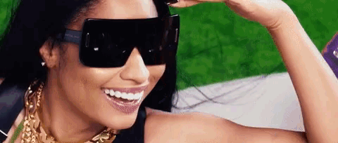 a woman wearing sunglasses and a gold necklace is smiling and looking at the camera .