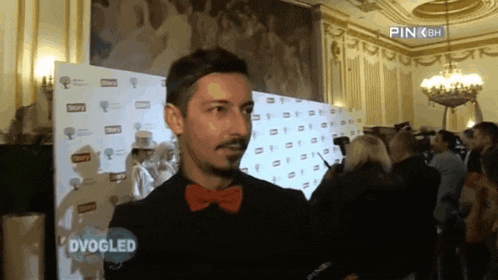 a man wearing a red bow tie is being interviewed by a pink bh reporter